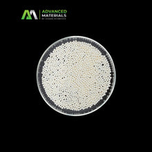 Top-down view of a clear petri dish filled with small white and black spherical particles, centered on a black background with the Advanced Materials by Vivara Scientific logo in the upper left.